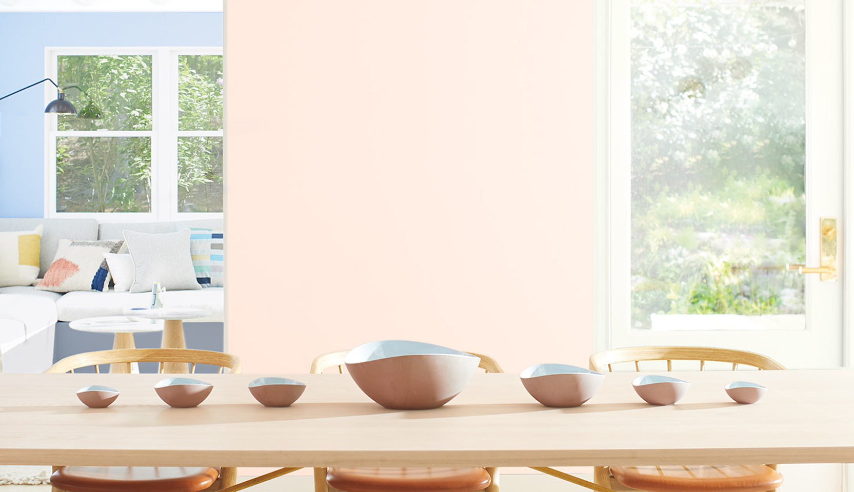 Light pink-painted dining room walls with a long wooden table, matching chairs and bench seating.
