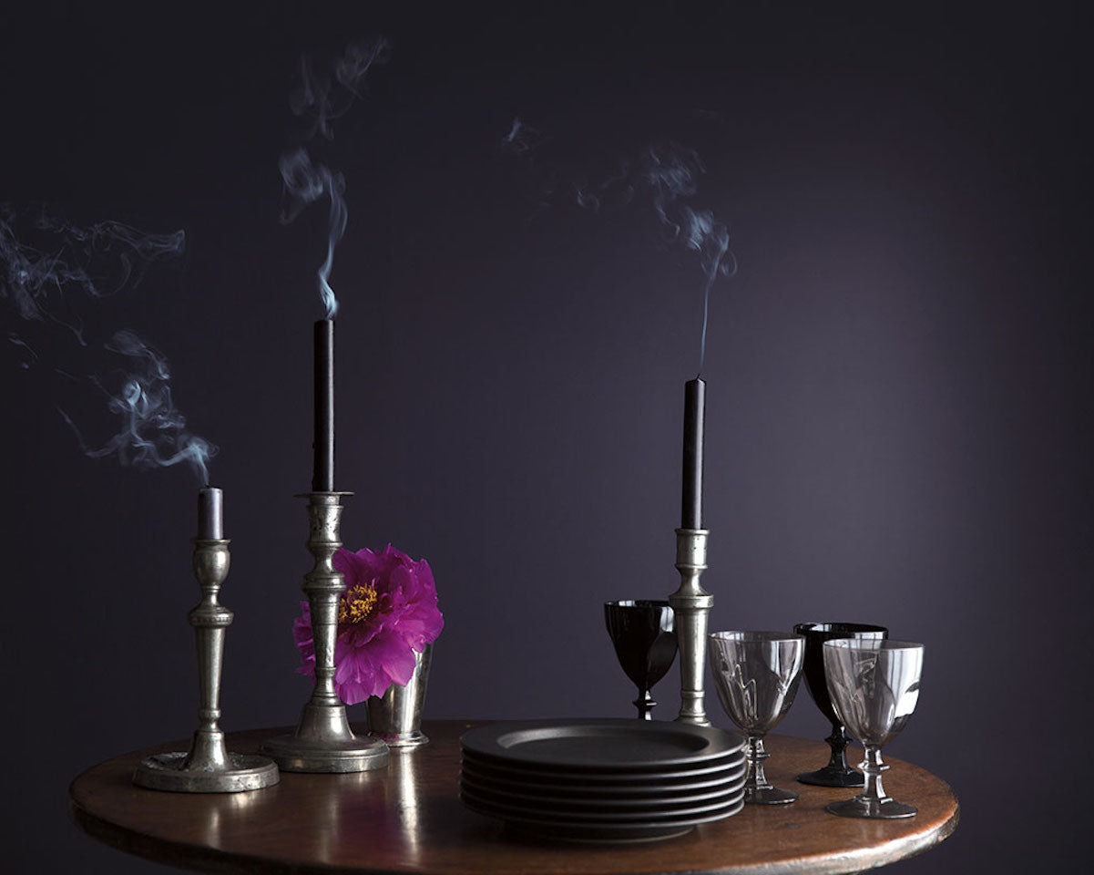 A wooden table with glasses, dishes, and candles in front of a dark purple wall.
